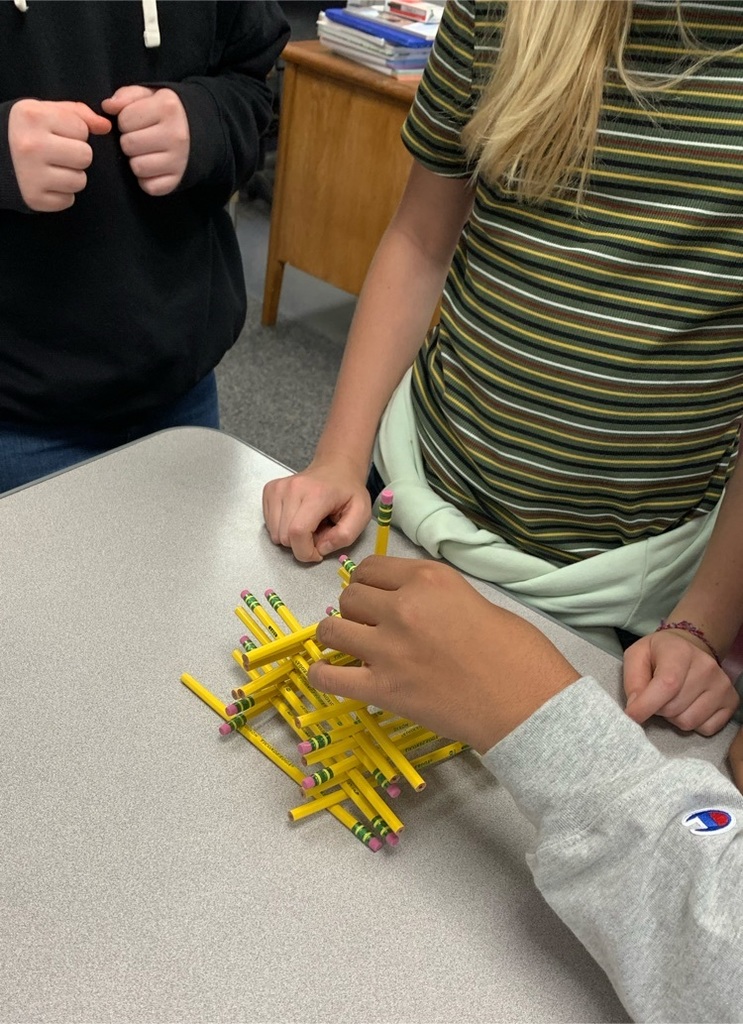Three students stack pencils. The stack is leaning slightly to the right and may fall soon.