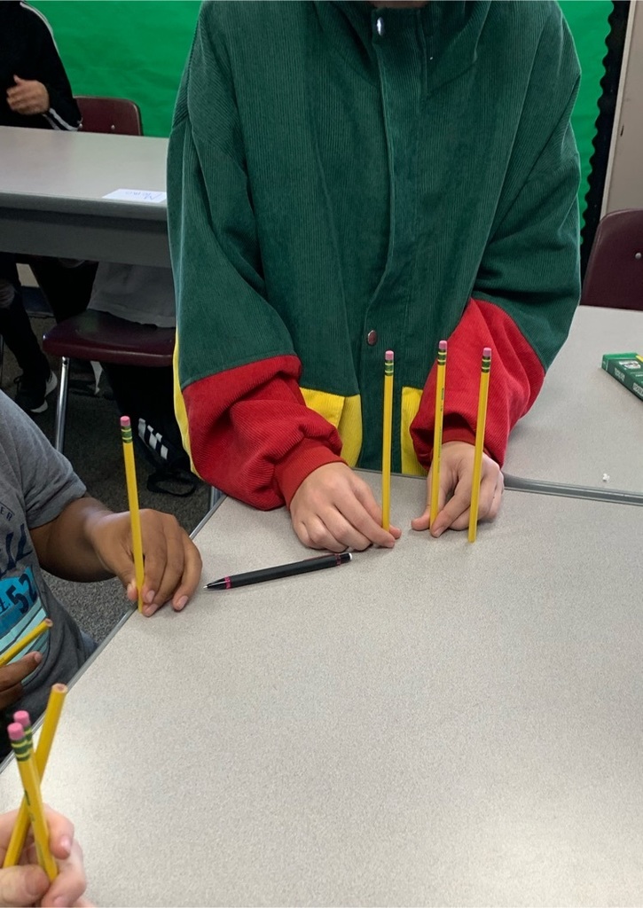 Two students have stood 4 pencils vertically. The pencils themselves are not connected or touching the other. 